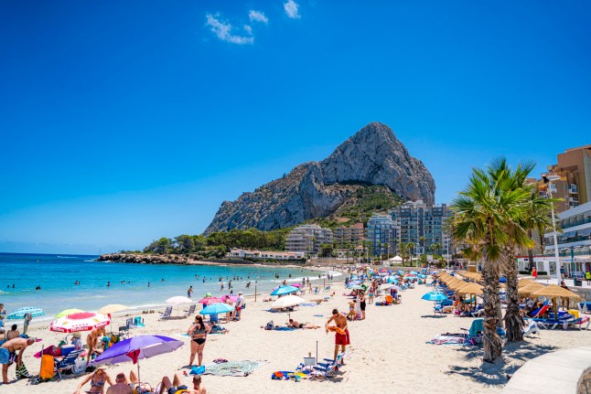People enjoying sun and beach with Penon de Ifach at background. Calp is a popular summer time vacation destination for tourist coming mainly from Germany and England and local retreat for Spanish.