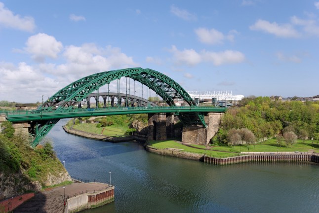 A view of the green Wearmouth Bridge over a river in Sunderland, England, on a bright day.