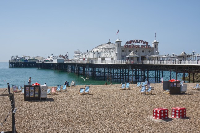 Brighton Palace Pier and shingle beach at Brighton in East Sussex, England. With people enjoying the sunshine.