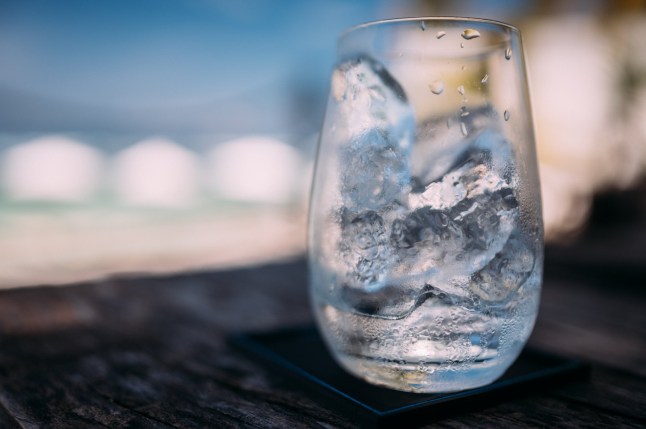 Refreshment in a glass of water filled with ice cubes, with a blurred seascape in the background.