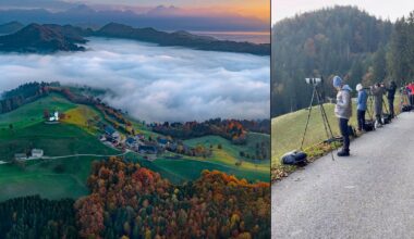 Aerial view of a village on green hills with autumn trees and low clouds; beside it, people with cameras and binoculars set up on a roadside, watching the landscape in cool weather.