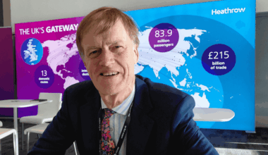 Stephen Timms smiling, in a suit and tie, sitting, with a map of the world behind him