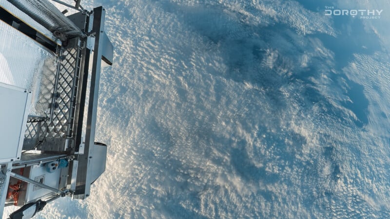 A satellite or spacecraft structure is visible on the left, overlooking a vast expanse of clouds over Earth, with sunlight casting shadows across the cloud tops. "THE DOROTHY PROJECT" logo appears in the top right corner.