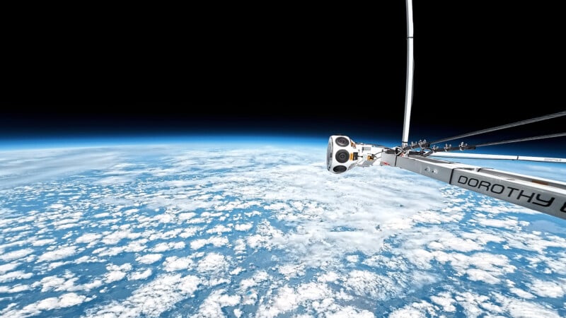 A camera attached to a metal arm labeled "DOROTHY" captures a view of Earth from high altitude, showing the curved horizon, vast white clouds, and the dark expanse of space above.