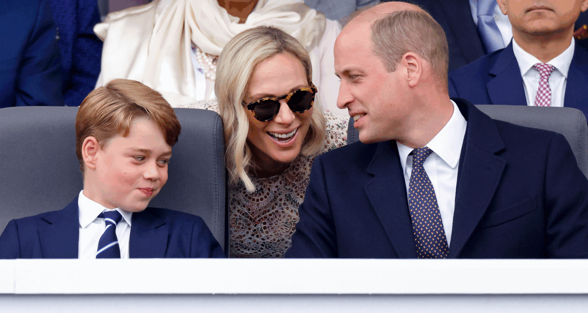 Prince George smirking as Zara Tindall leans over and talks to Prince William