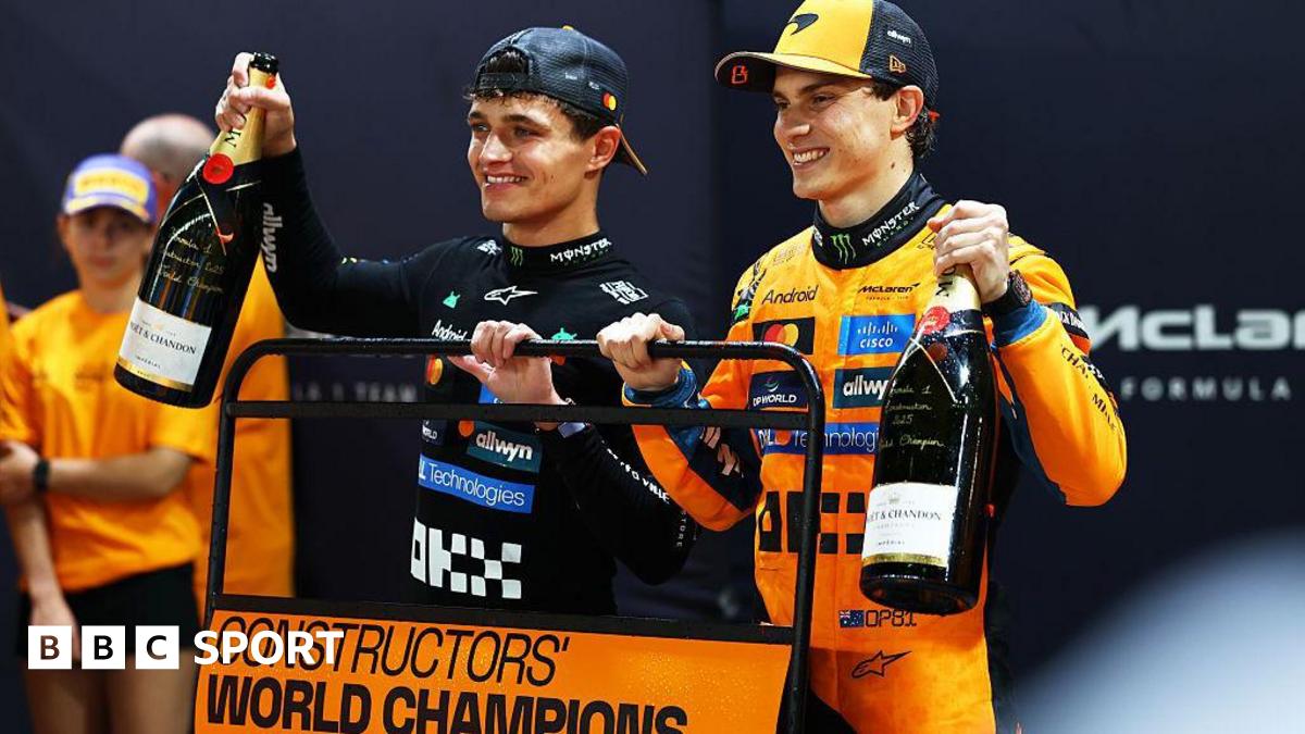 Lando Norris and Oscar Piastri celebrating after McLaren won the constructors' championship, holding up a board saying 'Constructors' world champions 2025'