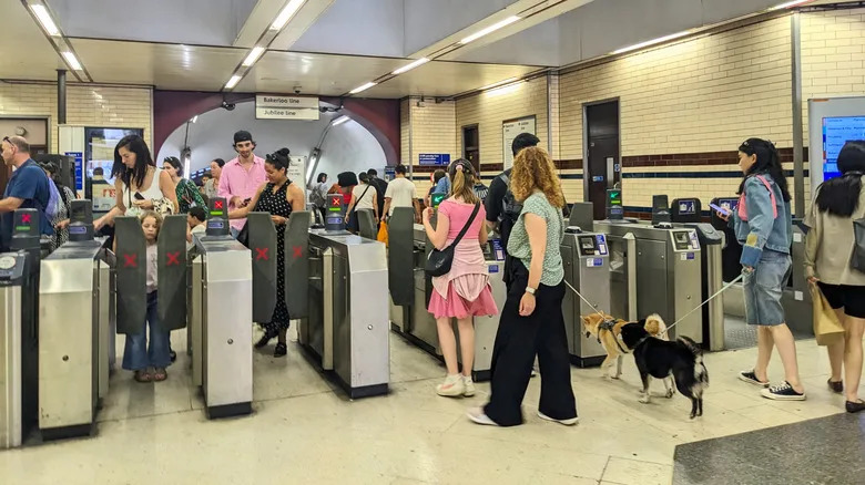A crowd of commuters entering and exiting the London Undergroun, tapping on and off with the machines.