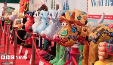Large statues of Aardman's Gromit character are lined up on a red carpet, positioned behind red tape. They are all painted with colourful designs, with the closest one a gold colour with gem stone paintings all over its face and body.