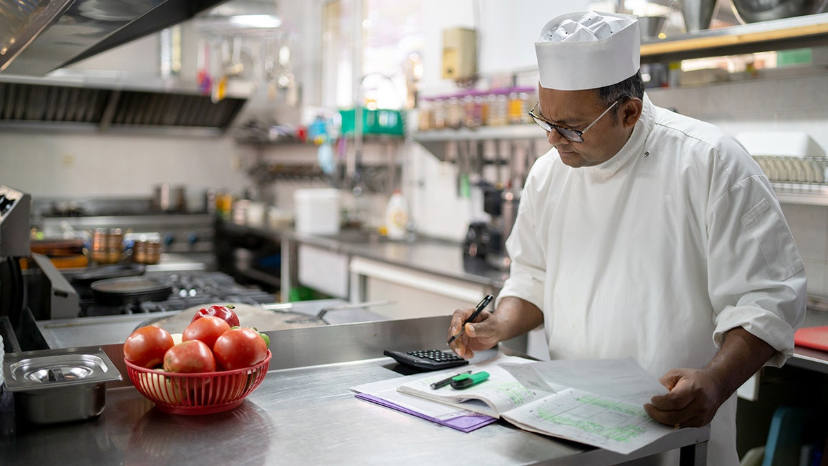 A chef uses a calculator in a commercial kitchen.