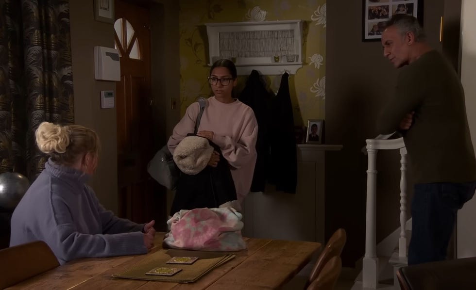 coronation street, bernie, asha and dev from left to right in dev's living house, with asha holding her belongings