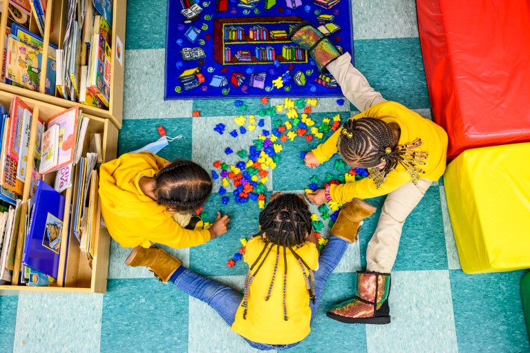A top-down view of three young children playing with colourful plastic bears in a classroom