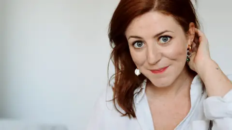 Catriona Byers  Catriona Byers has red hair and is wearing a white shirt. She is pictured against a white background.