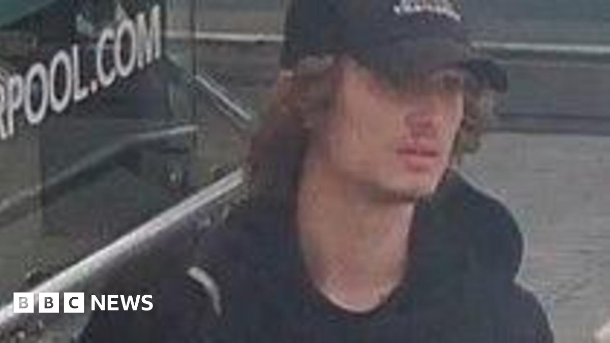 A CCTV image showing a young man with brown curly hair emerging from under a black baseball cap. He is wearing a black Monterrain hoodie