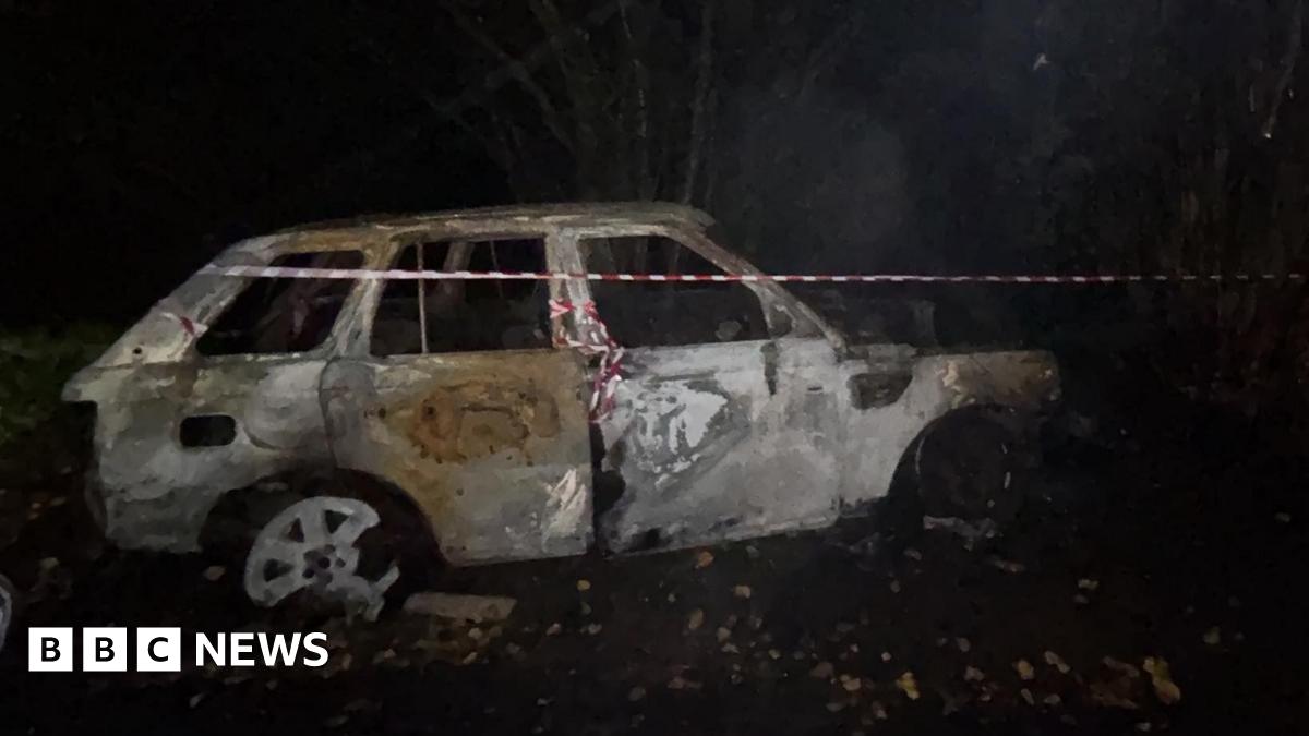 A burnt out white Range Rover in the dark with red and white tape around it