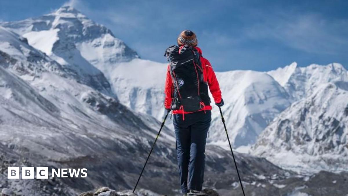 Hikers walking with winter coats and backpacks across a vast rocky plateau. In the background are snow-covered mountains.