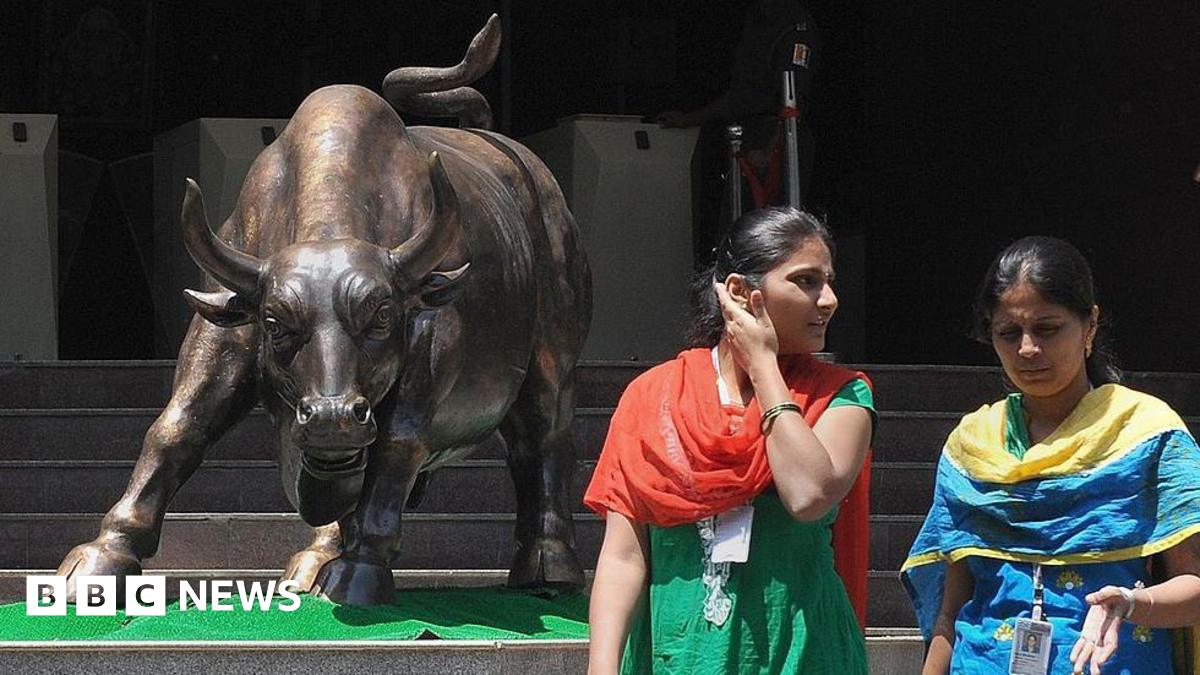 Indian women walk past the bronze bull outside the Bombay Stock Exchange, wearing traditional salwar-kurtas.