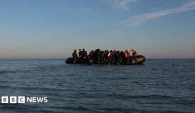Black inflatable dinghy in the English Channel. It is filled with people.