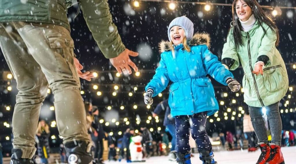family skating on ice rink with fairy lights above