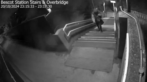 CPS Black and white CCTV footage shows a person walking up the steps into the station.