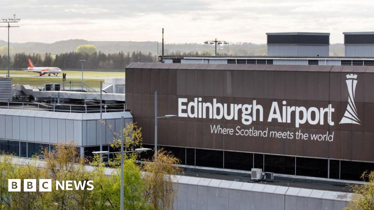 The exterior of Edinburgh Airport with an Easyjet flight landing on the runway in the top left hand corner of the shot