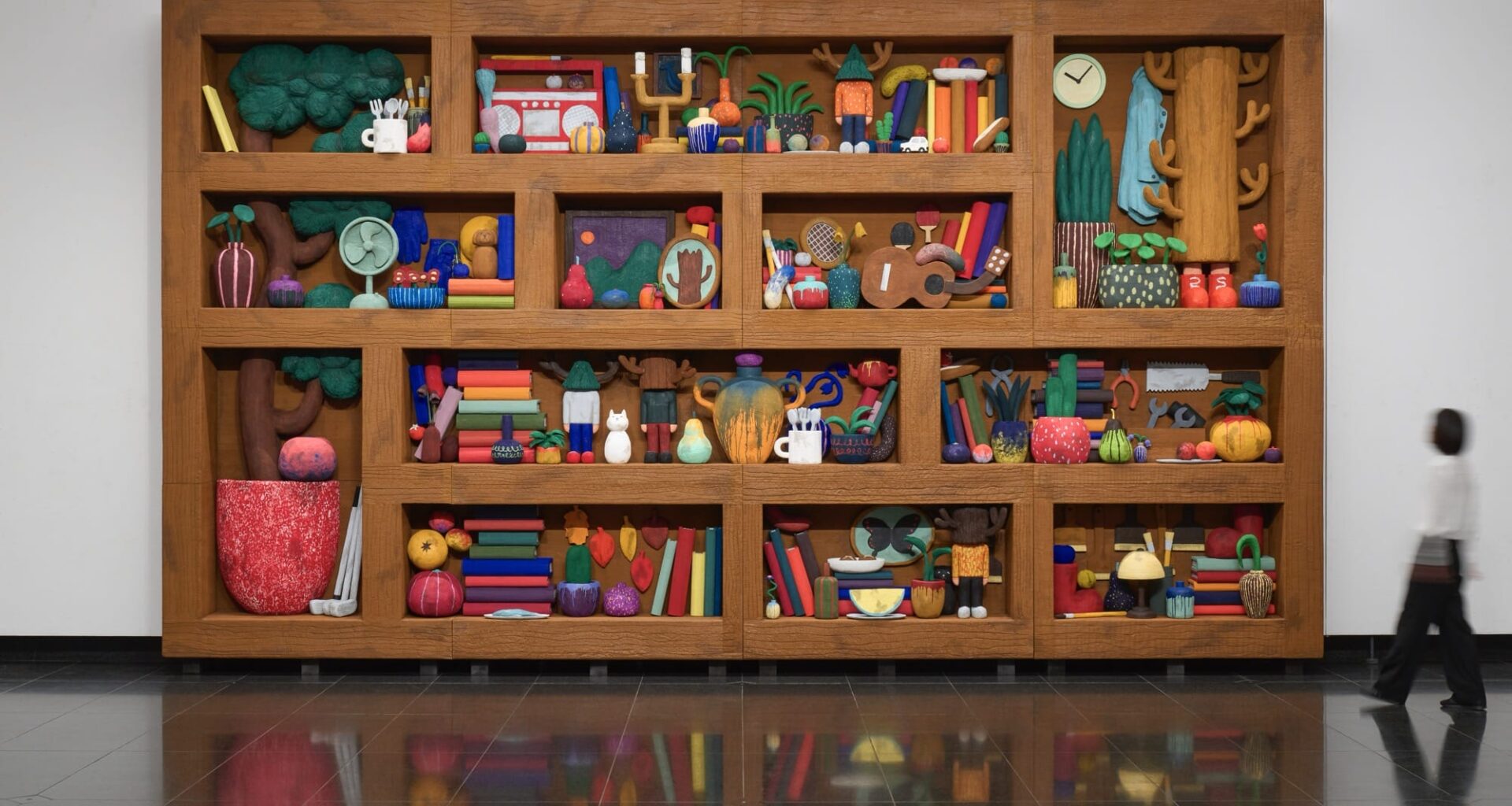 a sculptural installation by Yuichi Hirako of an oversized shelf filled with cartoonish domestic forms like vases, food, candlesticks, and other objects