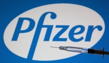 A medical syringe held in front of the Pfizer logo.