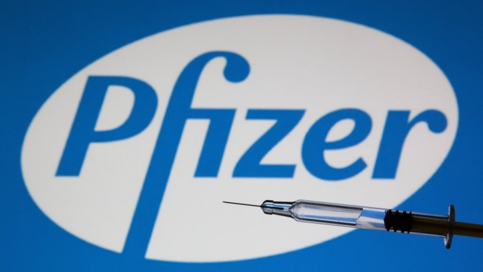 A medical syringe held in front of the Pfizer logo.