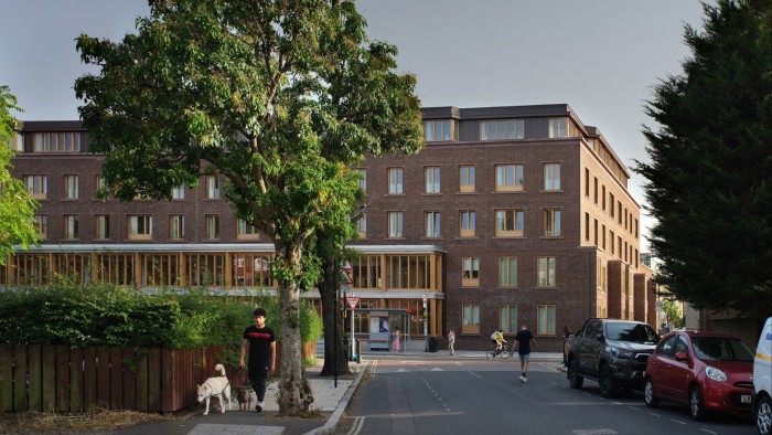 Appleby Blue Almshouse, a modern brick residential building with large windows, seen from across the street with pedestrians and trees in front.