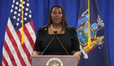 Letitia James speaks at a podium with the New York state seal, flanked by U.S. and New York state flags.