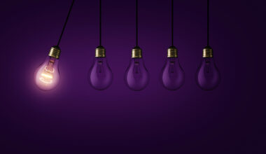 Creative light bulb lights up other extinguished light bulbs on a dark purple background, concept. Leadership, creative idea. Think differently. Start up