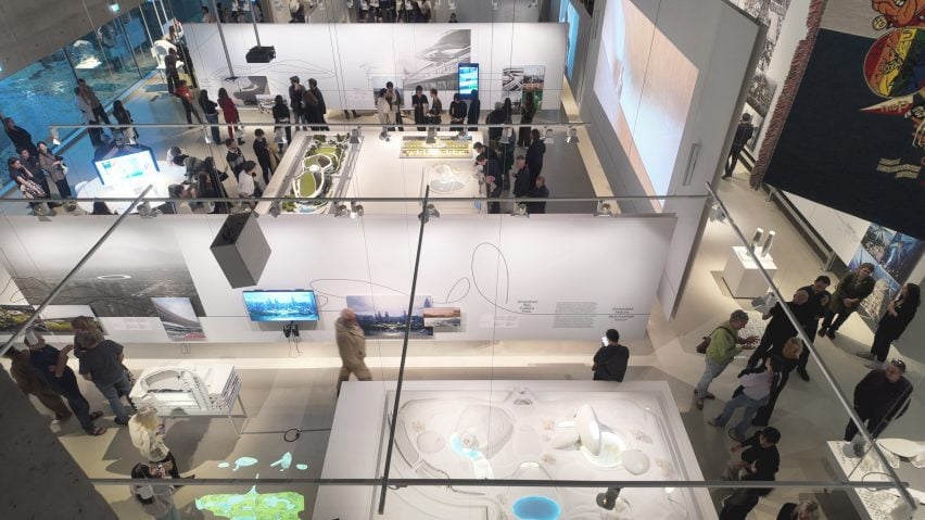 A wide shot of the exhibition hall at the Nieuwe Instituut showing large-scale models, screens and visitors