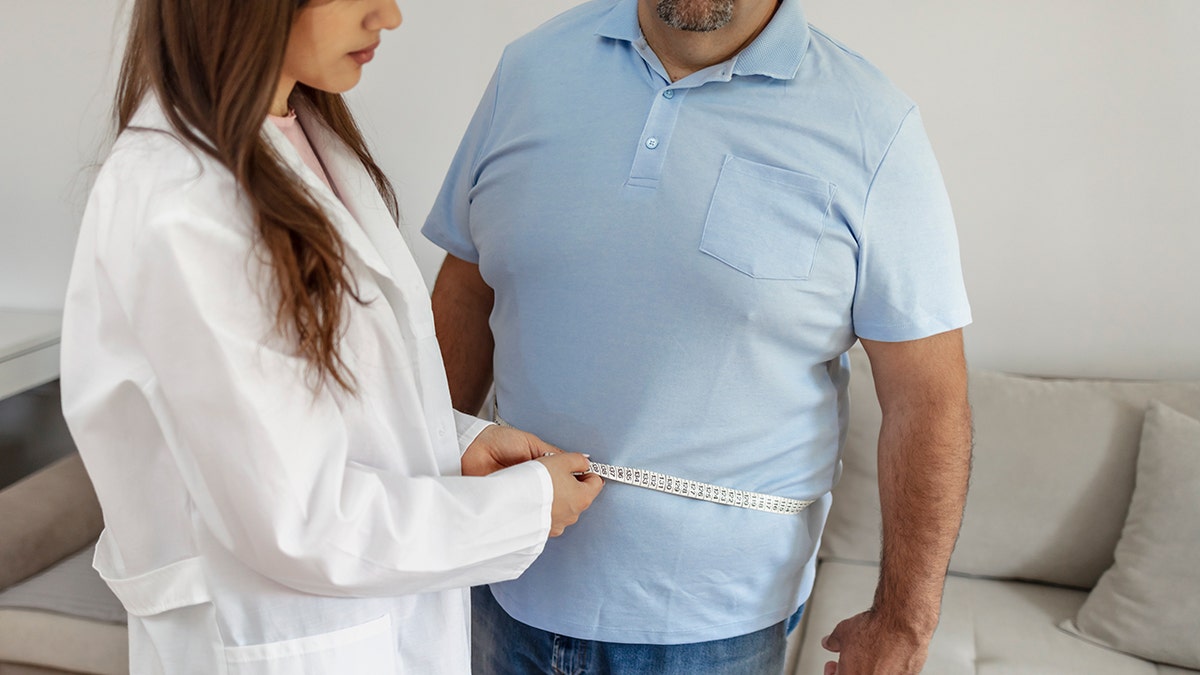 Female doctor measures obese male patient.