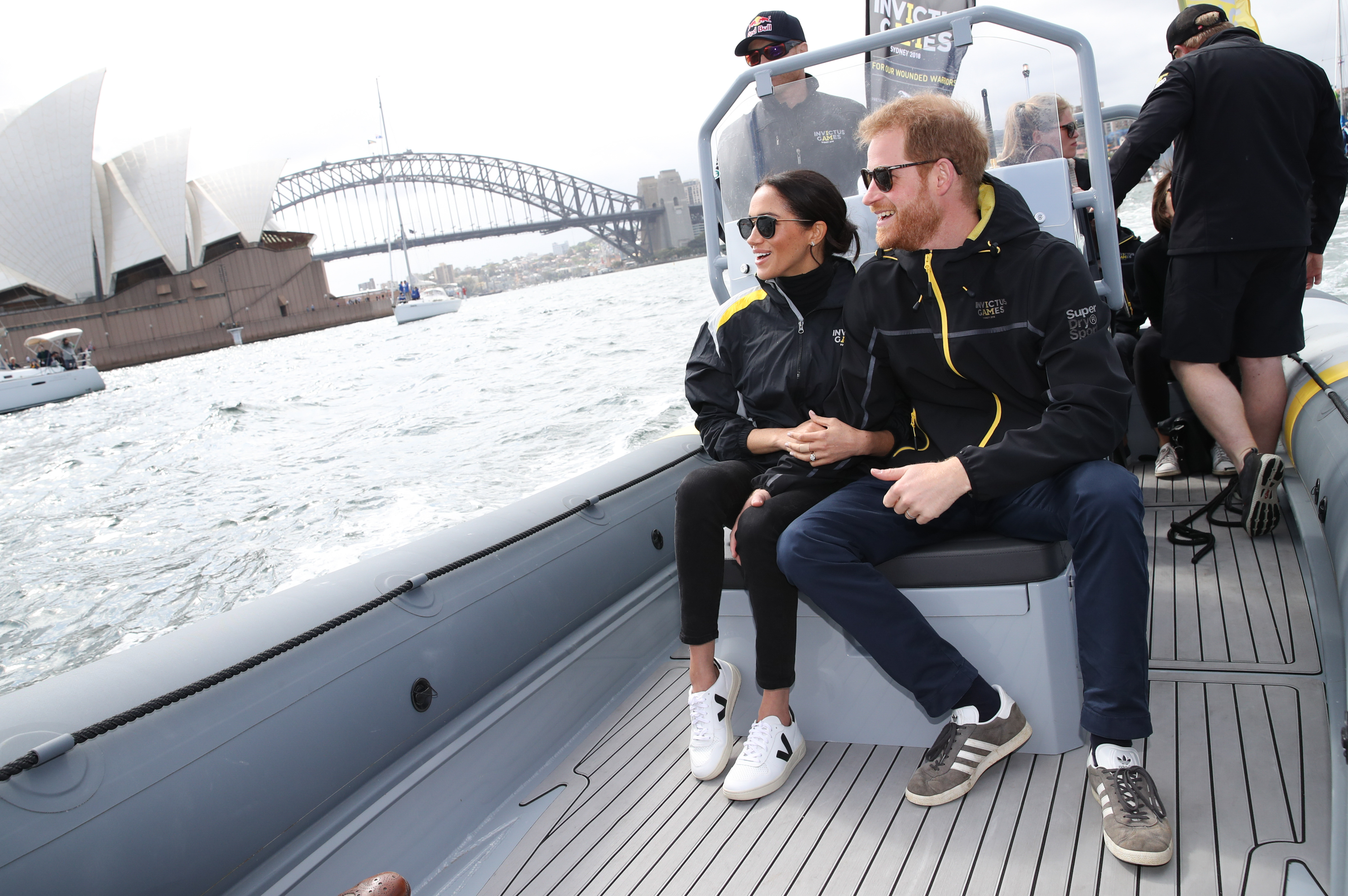 Meghan Markle and Prince Harry sitting on a boat wearing sneakers and jeans