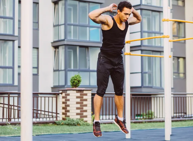 Jump up burpee. Sport exercises. Stage and release of squat. Exercises with free weight. Mixed race black man workout jump exercise on sport ground outdoor with urban cityscape on background.
