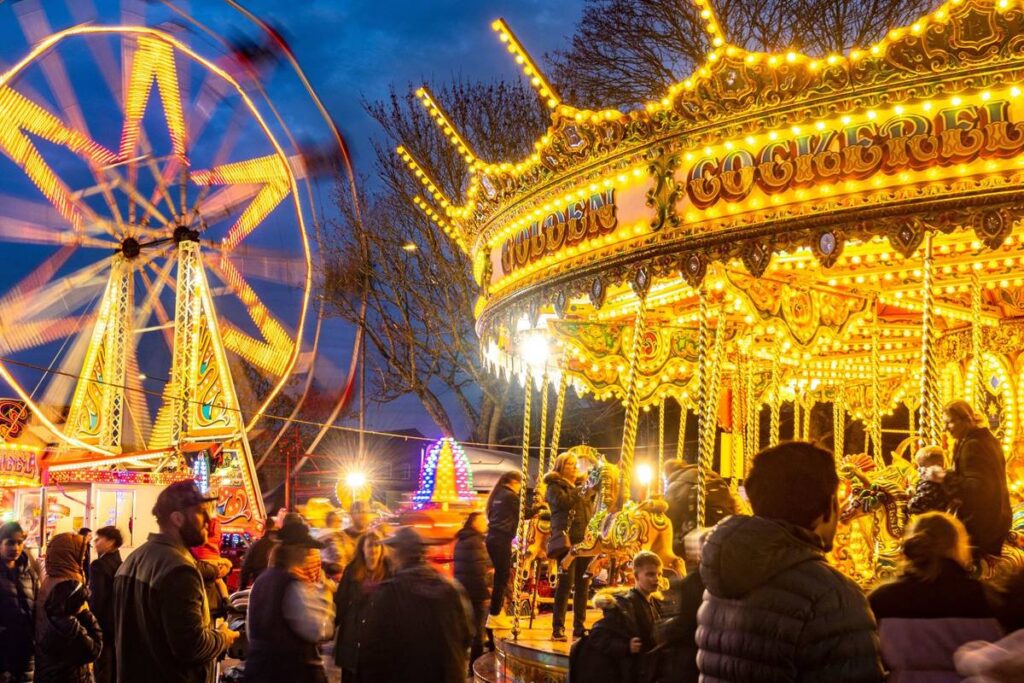 Worcestershire,England-November 29 2024: Members of the public watch and enjoy a brightly lit funfair rides,with carousel horses and big wheel spinning round,at the yuletide festive Victorian Fayre.