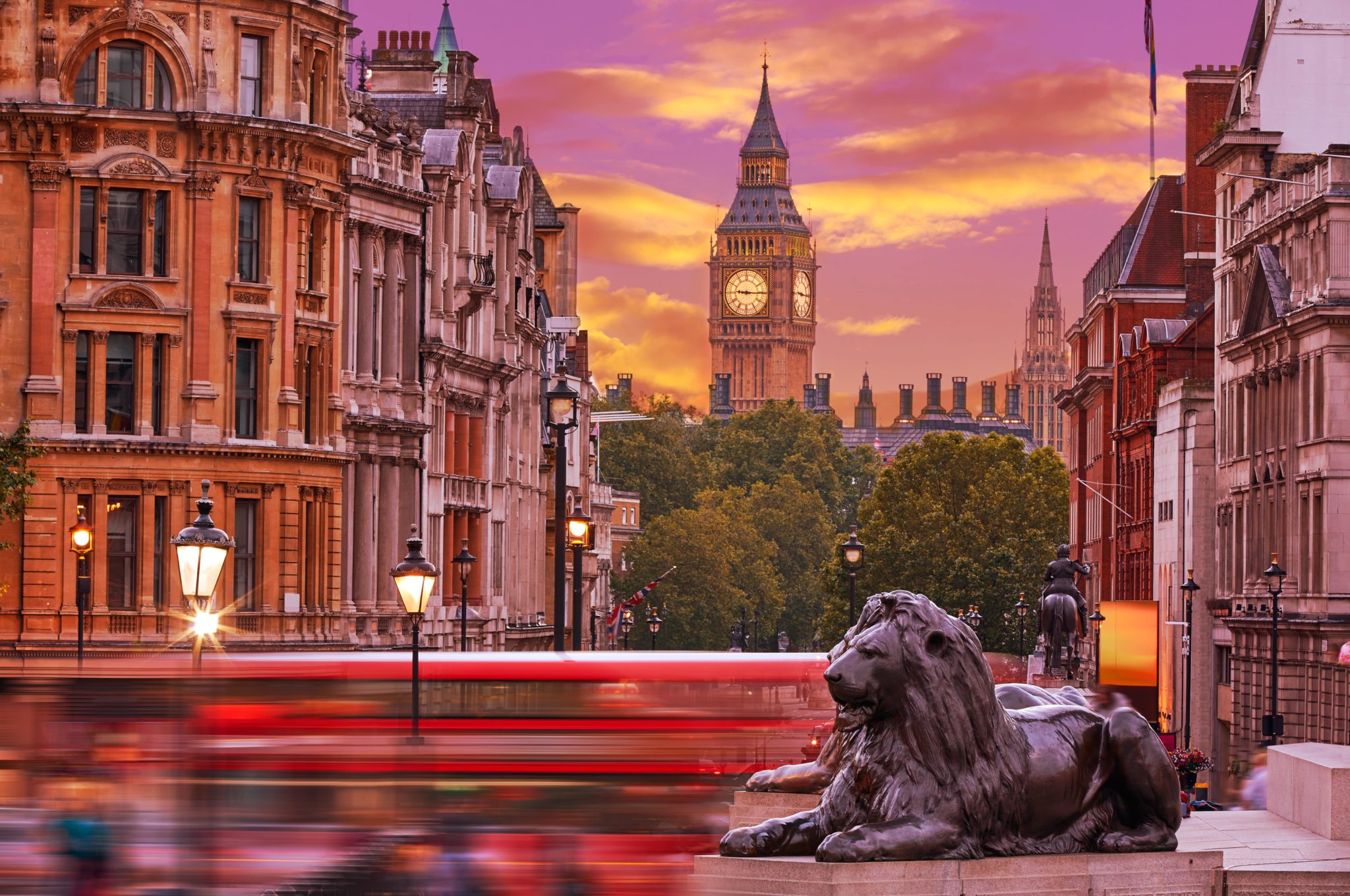 a pink and gold coloured sky over london at sunset, with big ben and the lion statues of trafalgar square visible, amidst rushing red buses