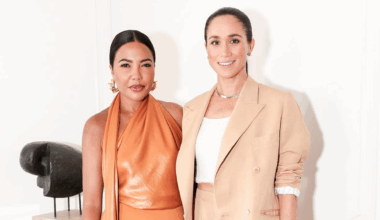 Meghan Markle wearing a beige suit standing with Emma Grede in an orange dress