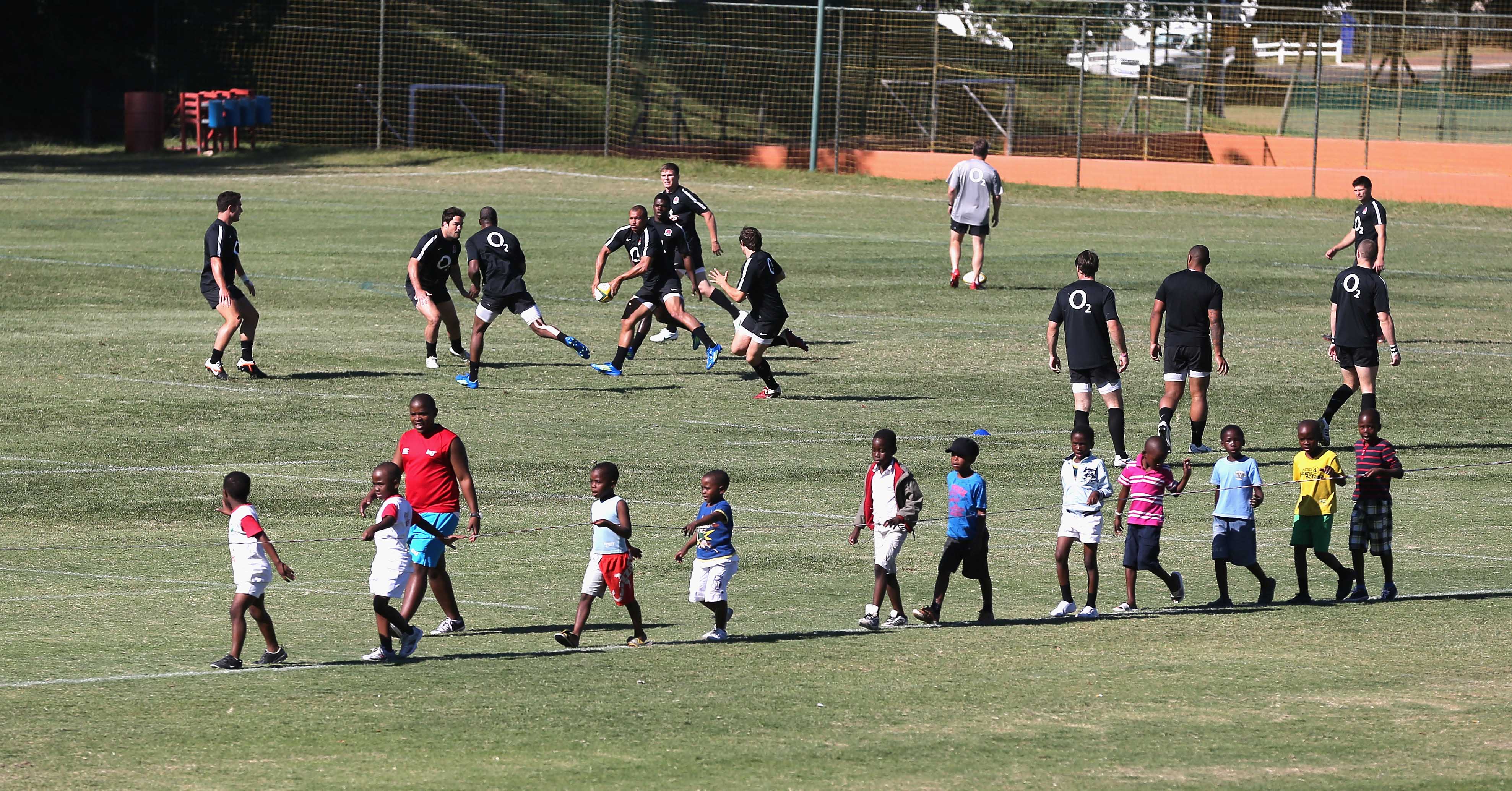 Jonathan Joseph passes the ball during an England rugby training session as local children look on.