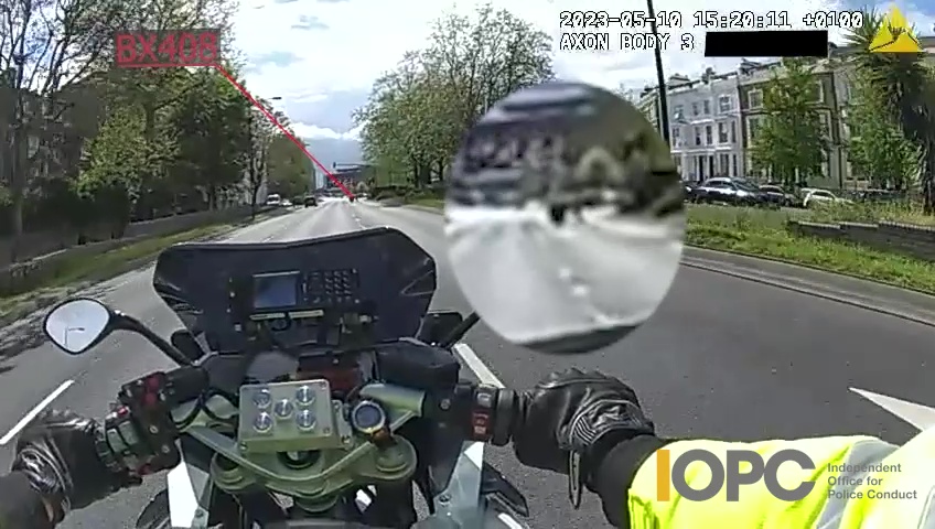Dash cam footage from a police motorcycle showing the road ahead, a gloved hand on the handlebars, and an IOPC logo.
