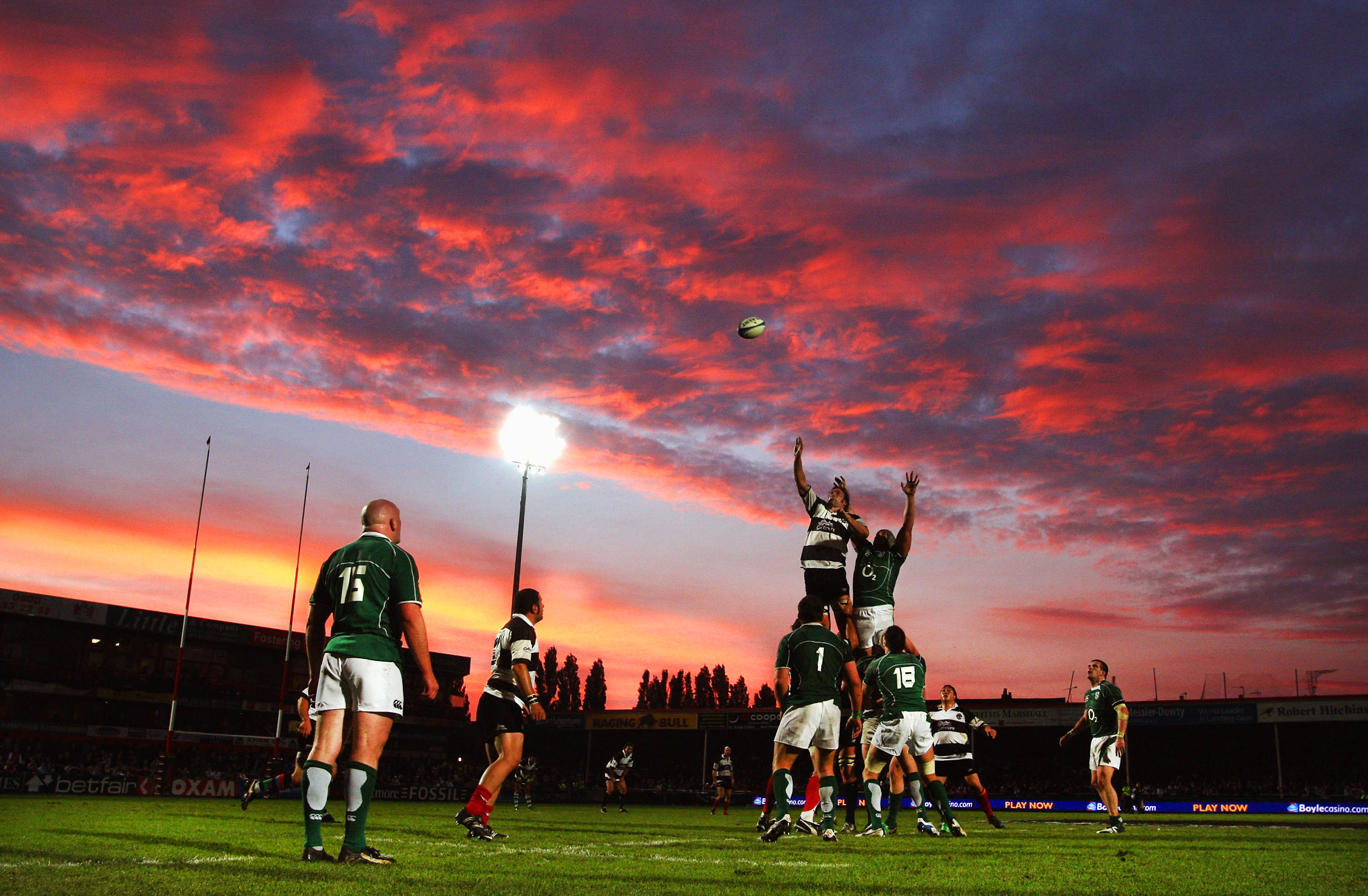 A rugby lineout with players jumping for the ball against a sunset sky.