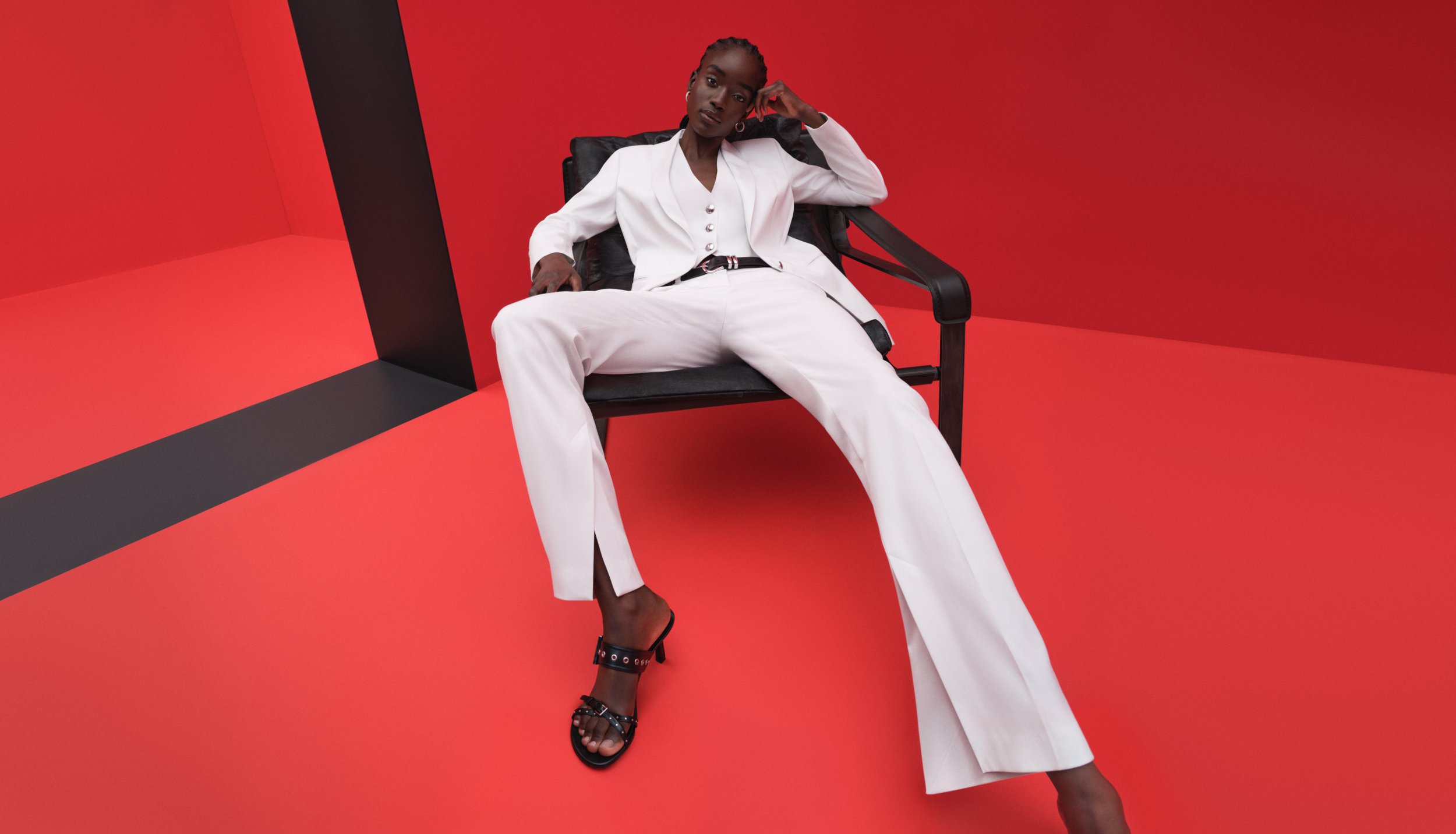 Woman in white suit sitting in a chair against a red background.