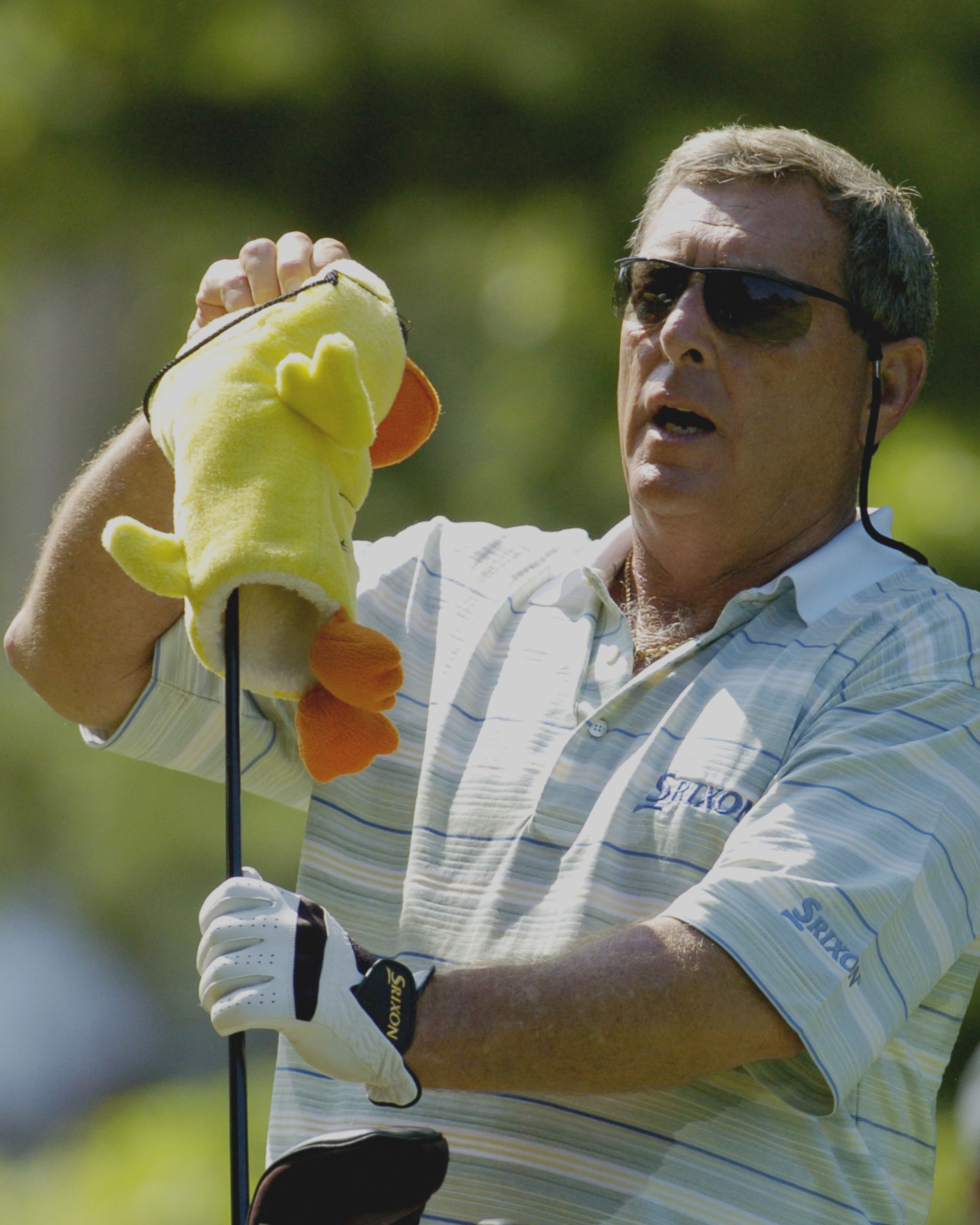 Golfer Fuzzy Zoeller inserting a yellow duck headcover onto his golf club.