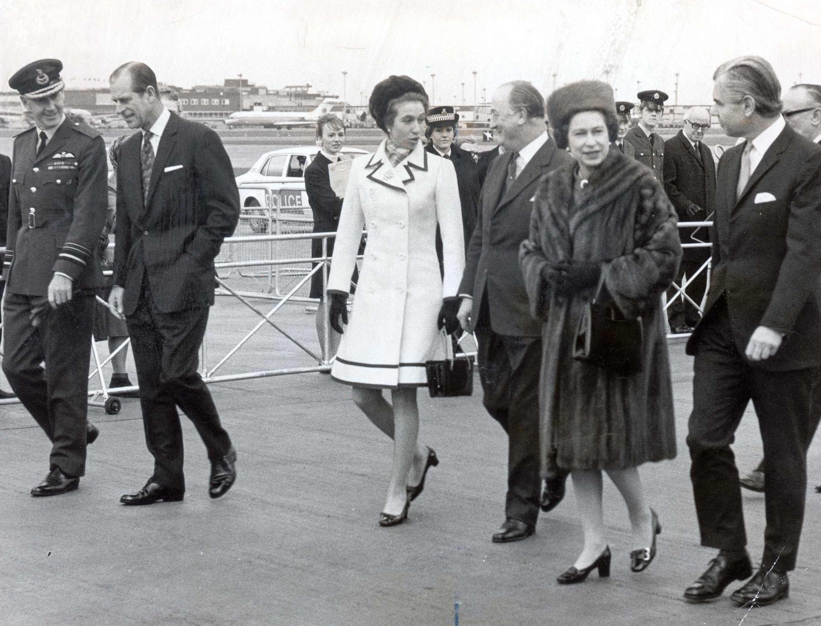 Princess Anne, Queen Elizabeth II, Prince Philip, and other officials walking at Heathrow Airport.