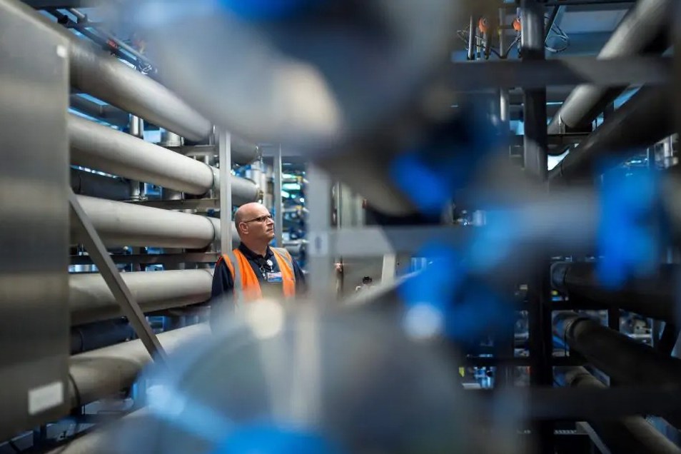Man in an orange vest and glasses looking up at pipes in a water treatment facility.