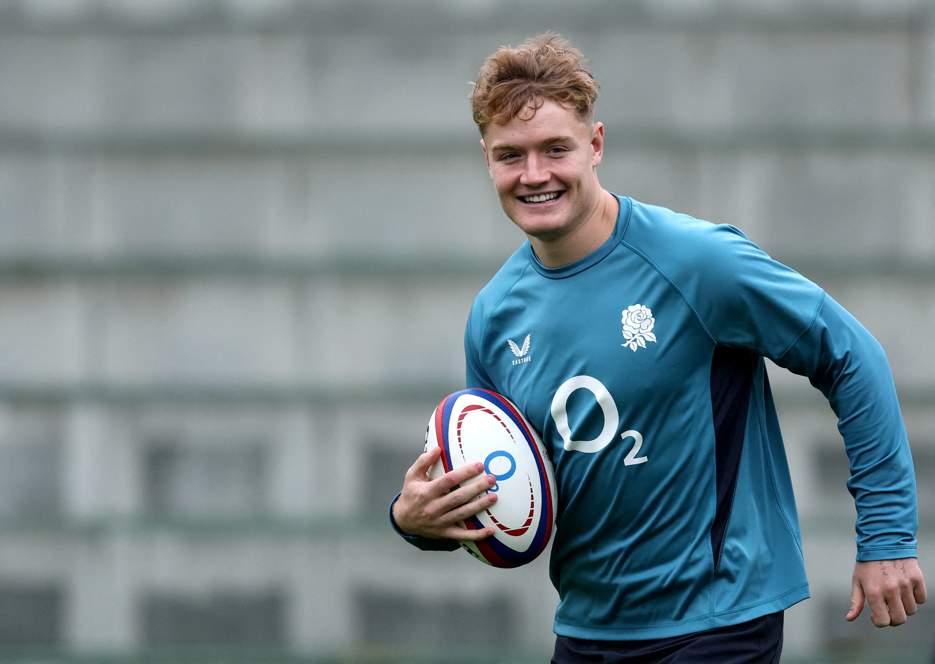 Fin Smith smiling and holding a rugby ball during England training.