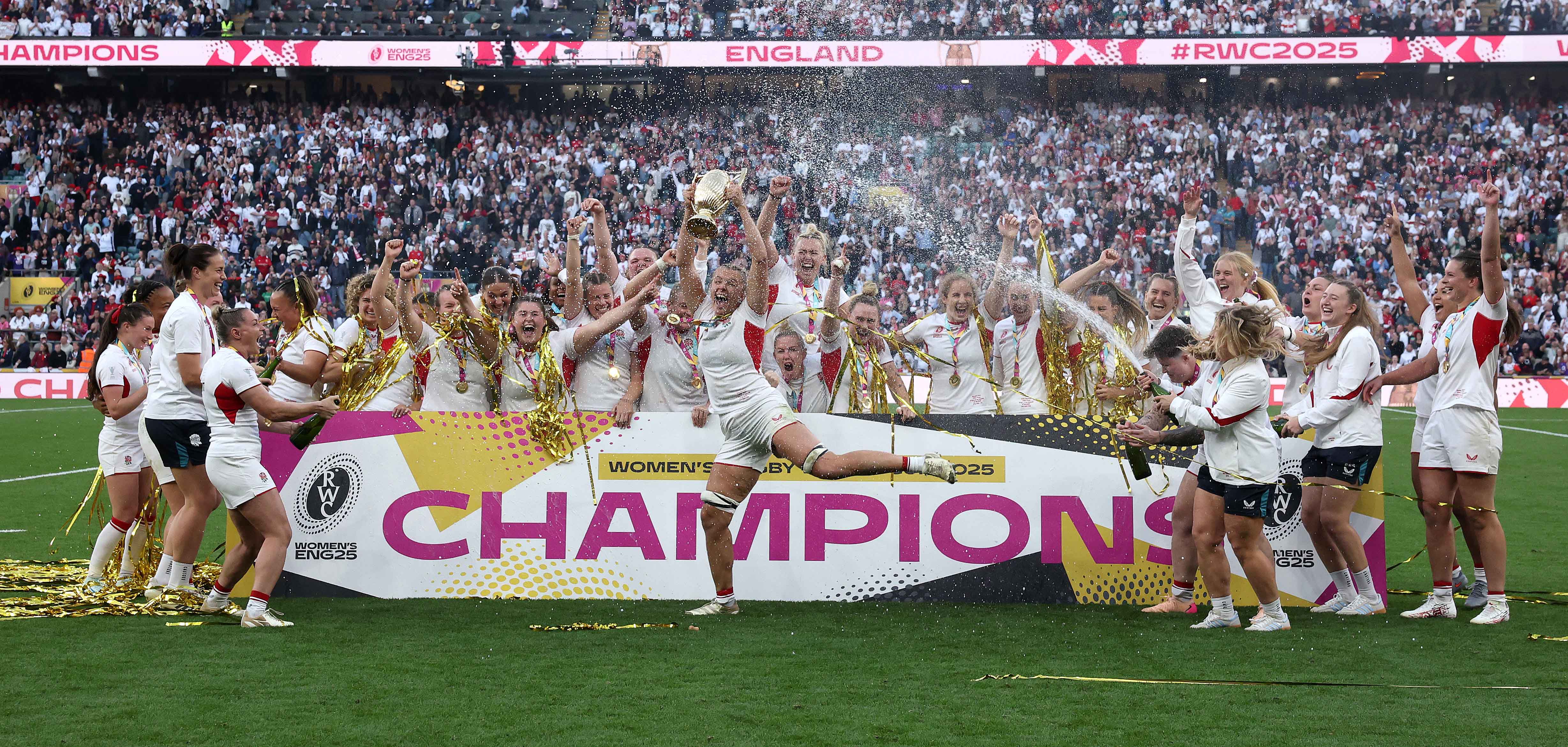 The England Women's Rugby team celebrating their victory at the 2025 World Cup final, holding the trophy and spraying champagne.