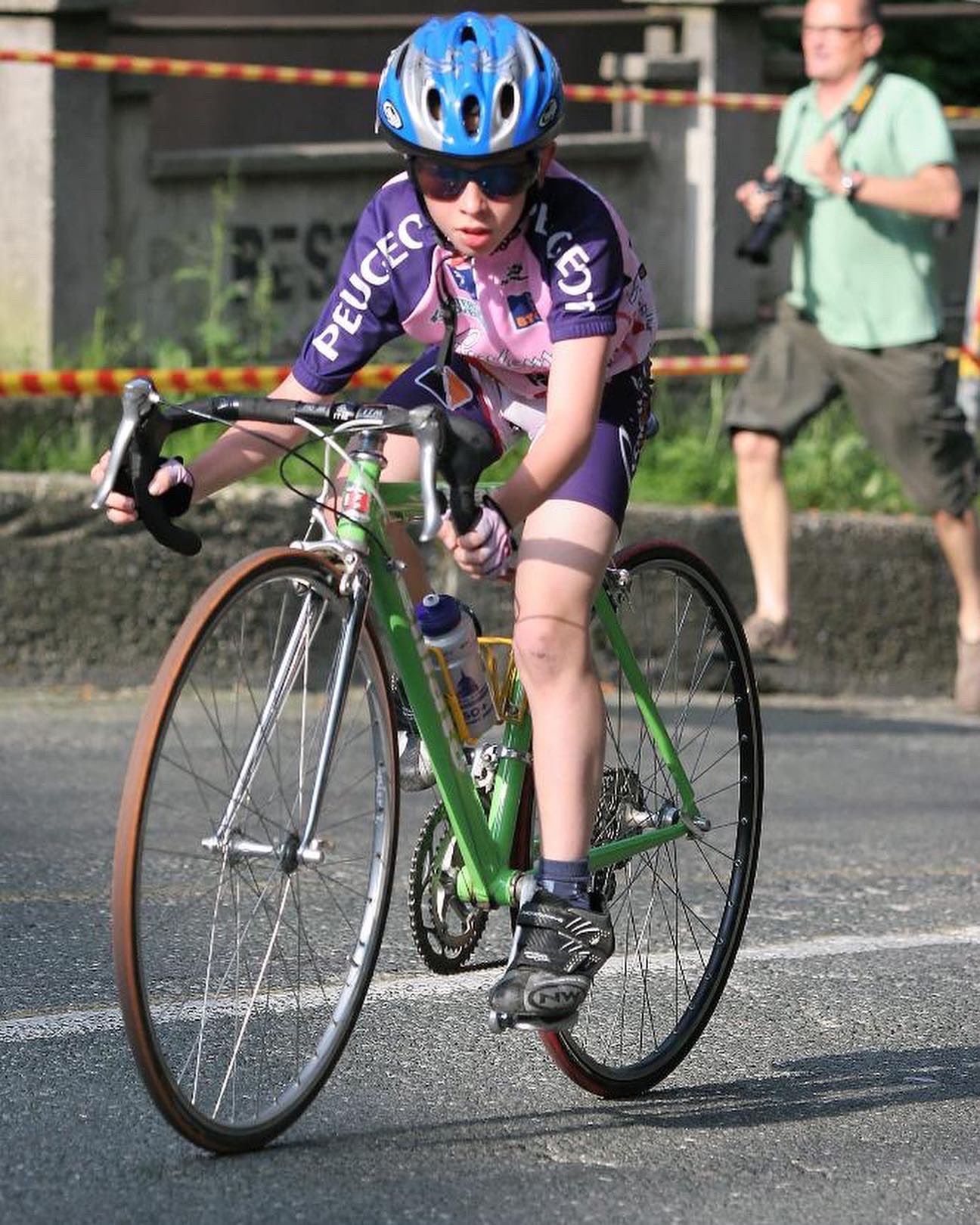 Young Tadej Pogacar in a purple and pink cycling jersey riding a green road bike.