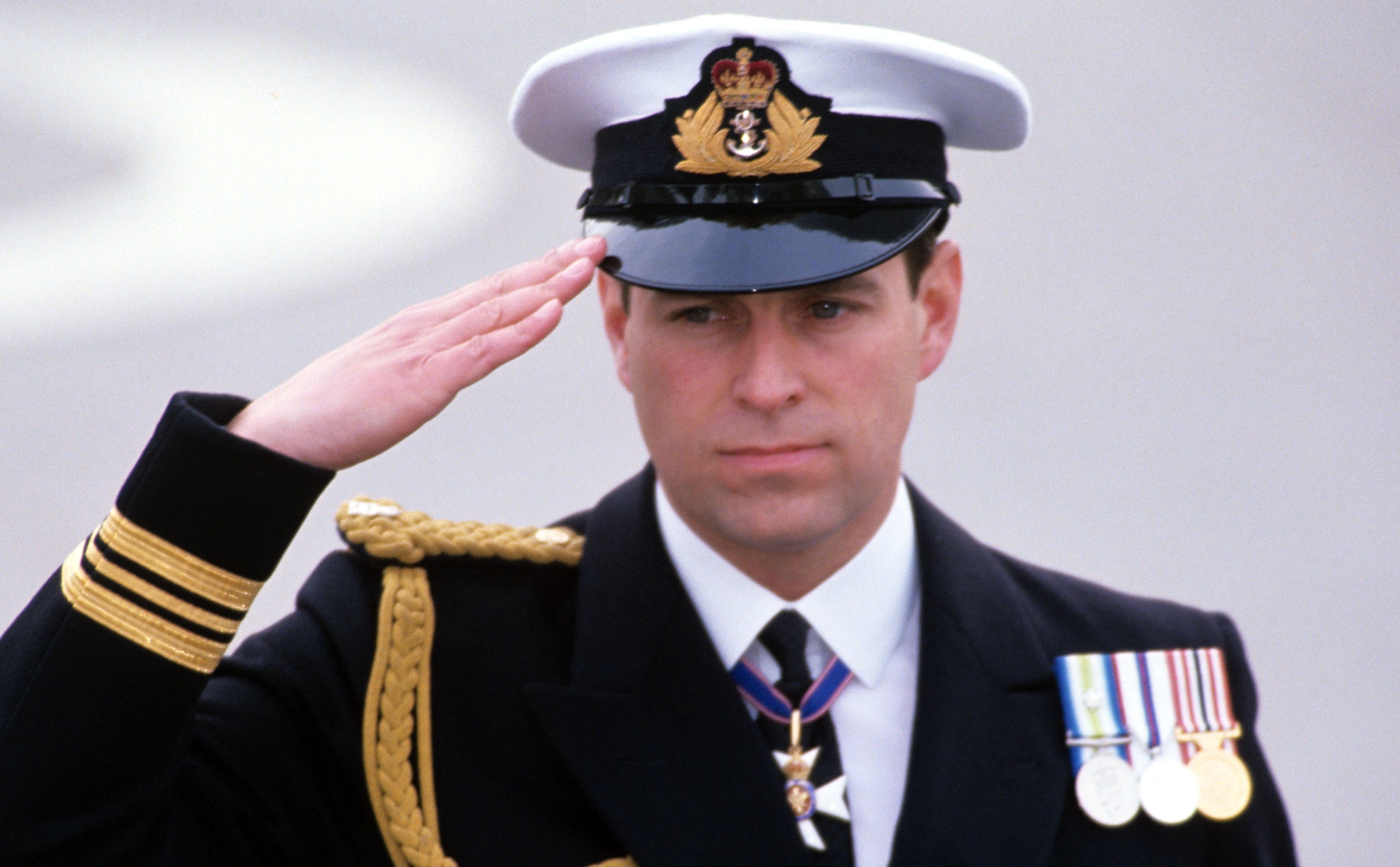 Prince Andrew, in naval uniform, saluting during a parade.