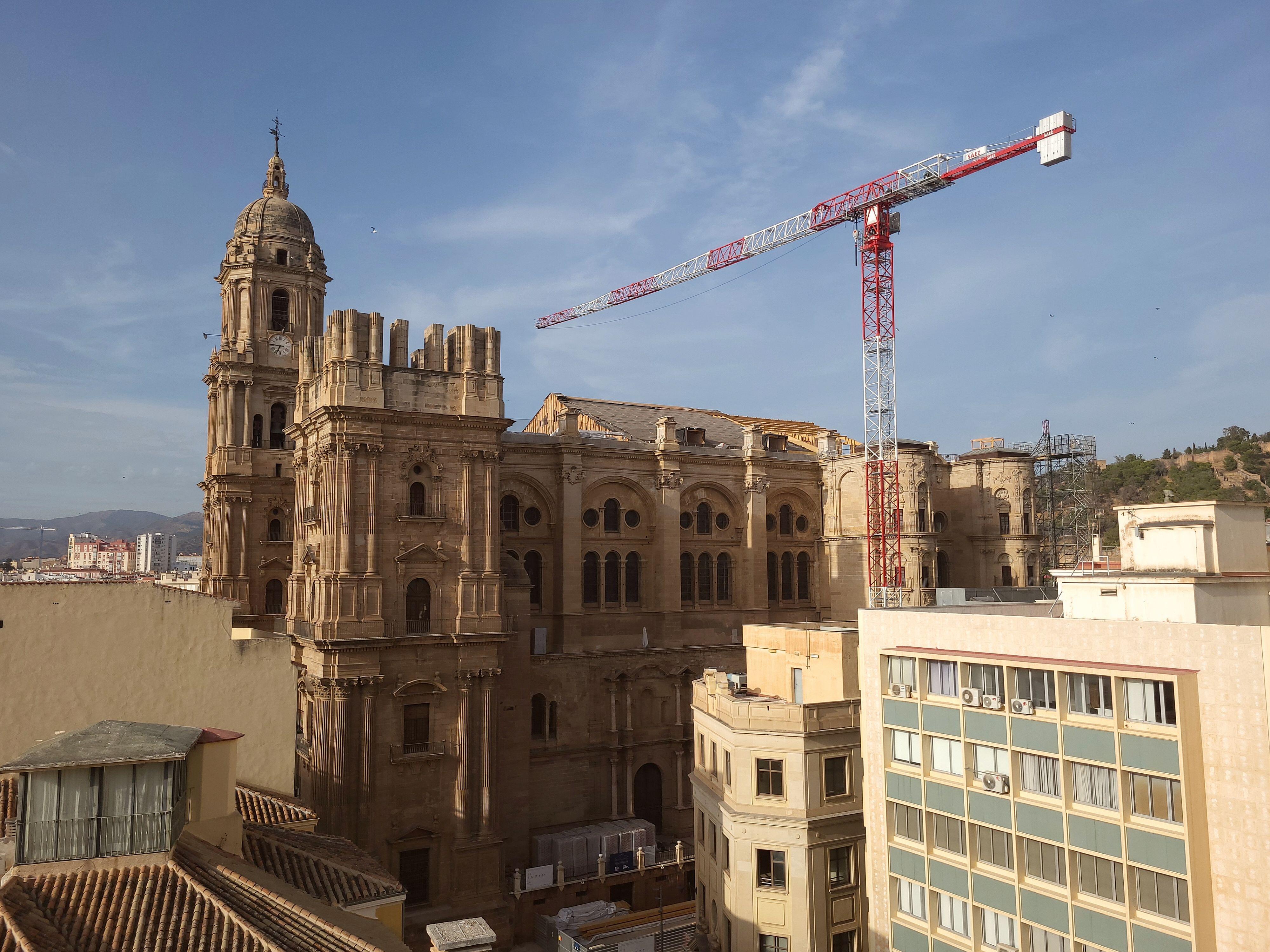 Malaga Cathedral under construction, with a large crane beside it.