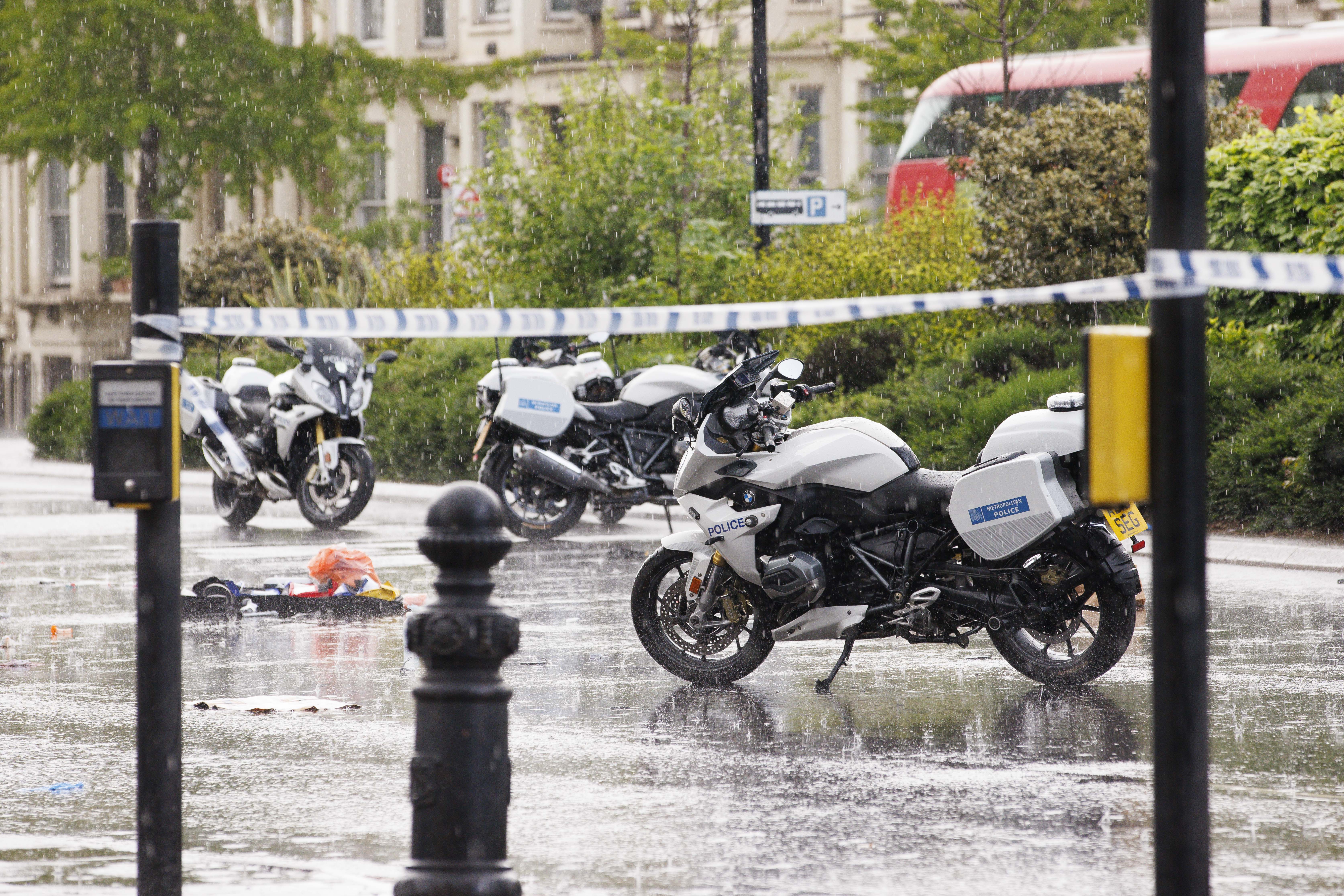 Police motorcycles inside a police cordon on a wet road, with medical equipment visible on the ground.